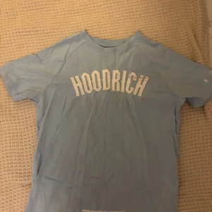 Ljusblå HOODRICH t-shirt i bomull - Snygg ljusblå t-shirt från HOODRICH med stort vitt tryck framtill och textdetaljer på ryggen. Klassisk rund hals och korta ärmar. Perfekt för en chill och avslappnad stil. Tillverkad i mjuk bomull som känns skön mot huden.