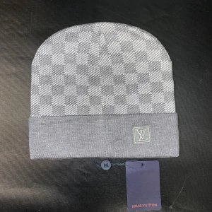 Grå rutig mössa  - Snygg grå rutig mössa med klassiskt rutigt mönster och uppvikt kant. Tillverkad i mjukt stickat material som håller dig varm och stilren under kyliga dagar.