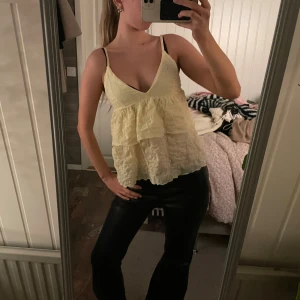 Volang topp - Säljer en ljusgul linnetopp från Gina Tricot med volanger och djup v-ringning. Toppen har tunna axelband och är tillverkad i ett lätt, krinklat material som ger en luftig känsla. Perfekt för varma dagar och somriga outfits. Har sytt upp banden lite då de var väldigt långa!