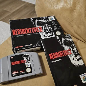 Resident Evil 2 (Nintendo 64) - Resident Evil 2 till Nintendo 64, komplett med originalkartong och manual. Kartongen har visst slitage i hörnen men spelet och manualen är i gott skick. En klassisk survival horror-titel från Capcom, perfekt för samlare.