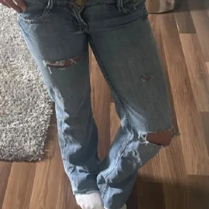 Blå jeans med slitningar från Il Dolce - Snygga blå jeans från Il Dolce med slitna detaljer och hål på benen. Insidan har ett blommigt mönster i midjan och bakfickorna är dekorerade med broderad text. 