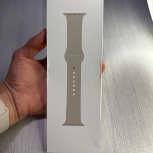 Apple Watch Sport Band 45mm – Starlight - Hejsan! Äkta Apple armband i färgen Starlight till salu. Själva bandet är helt nytt och oanvänt, men förpackningen är öppnad och något skadad. Passar Apple Watch 45 mm, storlek M/L. Passande handleder är 160-210 mm.  Butikspris: 595 kr  Mitt pris: 229 kr  Säg till om du undrar något :))