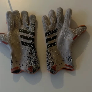 Adidas Predator målvaktshandskar - Säljer ett par Adidas Predator målvaktshandskar i grått och orange med svarta detaljer. Handskarna har en unik textur med gummitaggar på ovansidan och orange greppyta i handflatan. Perfekta för fotbollsmålvakter som vill ha stil och kontroll. Nypris 800