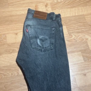 Levi's 501 svarta jeans - Klassiska svarta Levi's 501 jeans med rak passform och femficksdesign. Jeansen har en mörk tvätt, knappgylf och den ikoniska röda Levi's-taggen på bakfickan. Perfekta för en avslappnad och tidlös look.