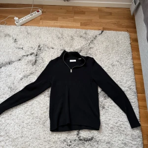 Svart ribbad stickad tröja med half zip - Svart stickad tröja från Jack and Jones med ribbad struktur och halv dragkedja vid halsen. Långärmad modell med hög krage, perfekt för lager-på-lager. Enkel och stilren design som funkar till allt.