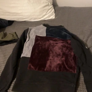 Patchwork sweatshirt från La Vichy - Unik sweatshirt från La Vichy med patchwork-design på ryggen i vinröd sammet, grått och mörkblått. Tröjan är svart med lång ärm och har coolt broderad detalj med fjäder och logga på ärmen. Säljs då den inte passar längre🤗