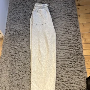 Ljusgrå mjukisbyxor med snörning - Säljer ett par ljusgrå mjukisbyxor med elastisk midja och snörning. Byxorna har två fickor fram och två bak, samt en loose passform med raka ben. Perfekta för chill dagar och riktigt sköna tack vare det mjuka bomullsmaterialet.