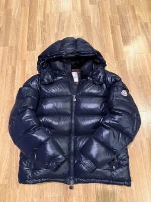 Moncler Maya Navy - Säljer min jacka då jag inte använder den, köptes för ca 2-3 år sedan och har använts varje vinter sedan dess. Den är puffy och väldigt skön och håller en varm hela vintern, har kört den utan tröja under men man kan köra med också. Finns Vit moncler påse som medföljer: Storleken är nummer 4 vilket motsvarar L. På dem två sista bilderna ser ni att det finns ett litet hål i luvan, hålet är inte helt igenom utan det är bara inre lagret som det gått hål i, Fråga  fler bilder för kunde inte ta alla. 