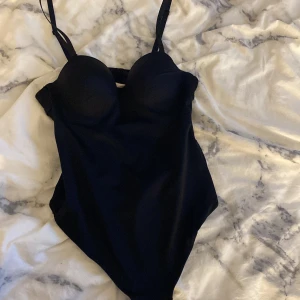 Svart body med bygel och kupor - Snygg svart body med vadderade kupor och bygel för extra stöd. Justerbara axelband och en cool cut-out detalj i ryggen. Oanvänd 