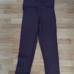 Lila leggings från Stillwell Sample - Snygga lila leggings från Stillwell Sample med hög midja och twistad detalj bak. Stretchigt syntetmaterial som sitter tight och bekvämt. Perfekta för träning eller chill. Enkel design utan mönster, med sömmar som ger en clean look. Lyfter rumpan.