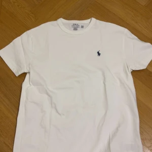 Vit Ralph lauren T-shirt  - Vit klassisk t-shirt från Polo Ralph Lauren. Tillverkad i mjuk bomull med en clean och stilren look, perfekt för dig som gillar enkel och snygg design. Den kan passa även M. Priset kan disk!