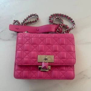 Quiltad rosa axelväska Steve Madden - Snygg quiltad axelväska från Steve Madden i stark rosa färg med silverfärgad kedja och coolt lås framtill. Väskan har en rektangulär form och är gjord i syntetmaterial. Perfekt för dig som vill sticka ut med en färgglad accessoar.