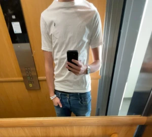 Vit t-shirt från Ralph Lauren - Vit t-shirt från Ralph Lauren med klassisk rund hals och korta ärmar. T-shirten har den ikoniska lilla Polo-loggan broderad på bröstet. Tillverkad i mjuk bomull för skön passform och stilren look. Perfekt till jeans eller shorts.