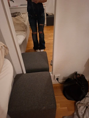 Blå bootcut jeans med slitna knän - Säljer ett par mörkblå jeans med bootcut passform och slitna detaljer över båda knäna. Jeansen har klassisk femficksdesign och är tillverkade i jeansmaterial. Perfekt för dig som gillar en avslappnad och edgy stil.