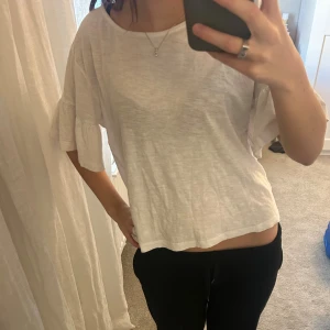 Vit blus med volangärmar - Säljer en vit blus med rund hals och korta volangärmar. Toppen har en loose passform och är tillverkad i ett lätt och luftigt bomullsmaterial. Perfekt för dig som gillar en enkel och chill stil med lite extra detalj på ärmarna.