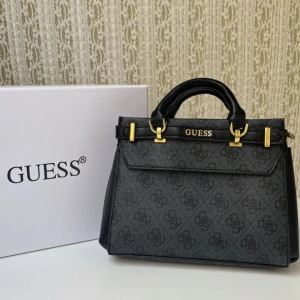 Guess handväska med gulddetaljer - Snygg handväska från Guess med guldfärgade metalldetaljer och logotyp framtill. Finns i svart och beige/brun med monogrammönster, samt helsvart. Väskan har flera fack, dragkedja och robusta handtag. Perfekt storlek för det viktigaste och stilren design.