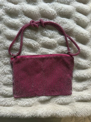 Glittrig rosa axelväska  - Snygg axelväska i rosaglitter över hela ytan. Väskan har en knytbar axelrem och stängs med dragkedja. Insidan är också rosa och har ett stilrent, modernt utseende som sticker ut. Perfekt för att addera lite extra bling till din outfit.