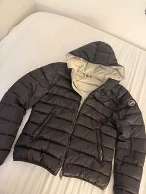 Svart dunjacka från Colmar - Snygg svart dunjacka från Colmar med quiltad design och huva. Jackan har dragkedja framtill, två sidofickor med dragkedja och en ljus insida. Perfekt för kalla dagar och har en modern, normal passform.