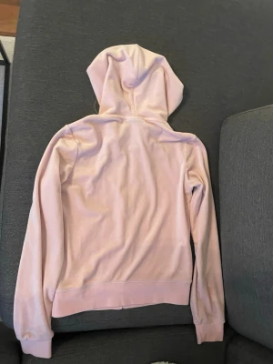 Ljusrosa hoodie med dragkedja - Säljer en ljusrosa hoodie med dragkedja framtill och fickor på sidorna. Hoodien har långa ärmar, ribbade muddar och en klassisk luva. Perfekt för en avslappnad och chill stil. Materialet känns mjukt och bekvämt, troligen bomullsblandning.