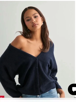 Mörkblå offshoulder  kofta med v-ringning - Mysig och trendig mörkblå kofta med djup v-ringning och knäppning framtill. Perfekt att bära off-shoulder för en avslappnad look. Passar snyggt till jeans och är ett måste i garderoben.