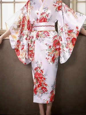 Japans klänning - Säljer en elegant kimono-inspirerad väst i vitt med färgstarkt blommigt mönster i rött, grönt och gult. Västen har breda ärmhål, omlott-design och ett midjeband som markerar midjan. Materialet är glansigt och känns lyxigt, perfekt för dig som vill sticka ut.