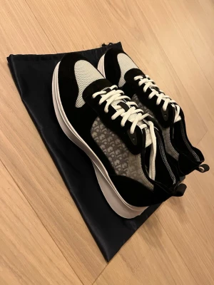 Svarta och vita sneakers - Snygga  sneakers i svart och vitt med klassiskt -mönster på sidan. Skorna har vit sula, svarta mockadetaljer, meshpartier och vita snören. Perfekta för dig som vill ha en exklusiv och trendig look.