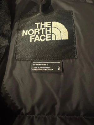 Svart dunjacka från The North Face - Säljer en svart puffer dunjacka från The North Face i storlek L. Jackan har en klassisk quiltad design, hög krage och dragkedja framtill. Perfekt för kalla dagar och riktigt skön att bära. Loggan syns tydligt på bröstet.