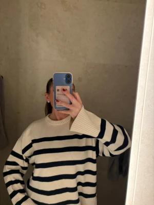 Randig stickad tröja i offwhite och marinblå - Snygg stickad tröja med breda marinblå ränder på offwhite botten. Tröjan har rund halsringning, långa ärmar och ribbade muddar. Perfekt för en avslappnad och trendig look.