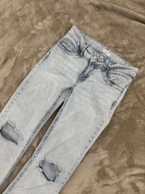 Ljusblå ripped jeans med broderade fickor från Nelly - Snygga ljusblå jeans med slitningar på knäna och unika broderade detaljer på bakfickorna. Jeansen har en klassisk femficksmodell och är tillverkade i mjuk bomullsdenim. Perfekta för en avslappnad och trendig look. 