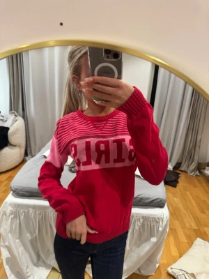 Rosa och röd stickad tröja GIRLS - Cool stickad tröja i rött och rosa med texten 'GIRLS' över bröstet. Tröjan har rund halsringning, långa ärmar och ribbade muddar. Perfekt för dig som vill sticka ut med färg och statement.