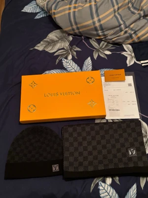 Louis Vuitton svart halsduk Damier - Snygg svart halsduk från Louis Vuitton i klassiskt Damier-mönster med LV-logga i hörnet. Halsduken har en stilren design och är tillverkad i mjukt material som känns lyxigt. Perfekt accessoar för dig som vill ha något exklusivt och tidlöst.