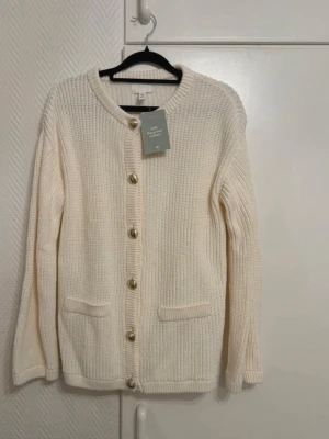 Krämvit stickad kofta från H&M - Oanvänd kofta med prislapp. Slutsåld. Köpt i H&M. Storlek XS (passar även en S).