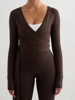 Brun tröja  - Säljer en mörkbrun omlottväst med långa ärmar och knyt i sidan. Västen har en djup v-ringning och är figurnära i modellen. Perfekt att styla över ett linne eller topp för en trendig look. Bara testad 