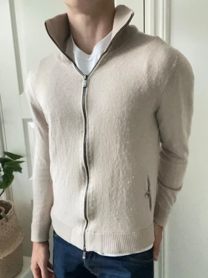 Massimo dutti full zip beige  - Massimo dutti full zip beige , väldigt hög krage vilket jag tycker är snyggt. Den är knottrig som ni ser men jag tar bort det ifall ni köper då jag har rätt verktyg osv för sånt. Modellen är 180 cm 75 kg och bär L