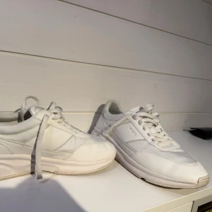 Vita sneakers från Axel Arigato - Stilrena vita sneakers från Axel Arigato med klassisk låg siluett. Diskret logga i guld på sidan och är tillverkade i skinn och syntetmaterial. Perfekta för dig som gillar clean stil.