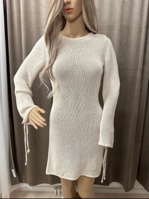 Vit stickad klänning med snörning ZARA - Snygg vit stickad klänning med lång ärm och snörningsdetaljer vid ärmsluten. Klänningen har en rak passform och är perfekt för dig som gillar en enkel men trendig look. Mjuk och skön att bära.