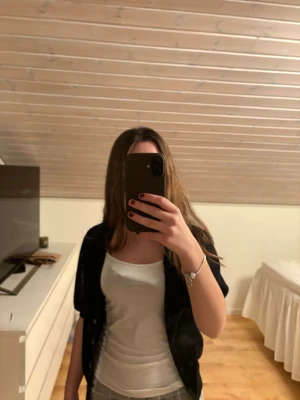 Svart kortärmad kofta med knappar - Svart kofta med korta ärmar och knäppning framtill. Koftan har en ribbad struktur och är lätt och luftig, perfekt att slänga över ett linne eller t-shirt. Enkel och stilren design som passar till många outfits.