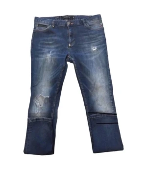 Blå croppade jeans med slitningar - Unika blå jeans med croppad passform och slitna detaljer framtill. Jeansen har klassisk femficksdesign, kontrastsömmar och broderad detalj på ena bakfickan. Perfekta för dig som vill sticka ut med en edgy streetstil.