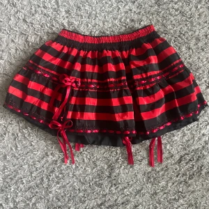 Röd och svart randig kortkjol med rosetter - Kort kjol fr Poizen. Onesize. Helresår i midjan. Helt ny.