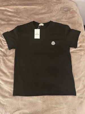 Svart Moncler t-shirt i bomull - Aldrig andvänd svart t-shirt från Moncler med klassisk rund hals och korta ärmar. Moncler-logga på bröstet och mjukt material i bomull som känns skönt mot huden. 