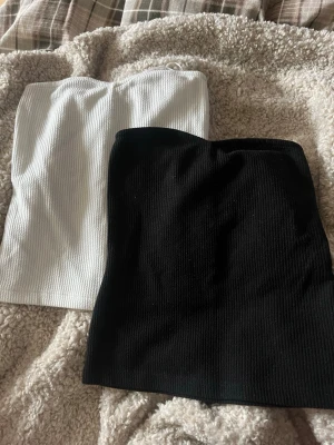 Ribbade svarta och vita tubtoppar - Två stilrena bandeau tubtoppar i ribbat material, en i svart och en i vitt. Perfekta att matcha med jeans eller kjol. Använd fåtal gånger🩷
