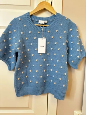 Blå stickad tröja  - Supersöt blå stickad tröja i helt nytt skick från Vila med korta ärmar och vita fluffiga prickar över hela