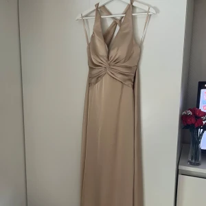 Champagnefärgad långklänning i satin - Elegant långklänning i champagnefärgad satin med omlott-detalj och knyt i midjan. Axelband som korsas i ryggen och sedan knyts som en rosett. Klänningen passar perfekt för bröllop eller bal. Använd endast en gång. Har dock fått några små repor på framsidan av klänningen, vet inte om man kanske kan fixa det på något sätt eller om man vill göra om den 🥰ordinarie pris var 1699 kr, säljer för 200 kr💗