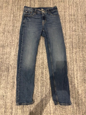 Blå raka jeans med klassisk passform - Ett par blå jeans med rak passform och klassisk femficksdesign. Jeansen har normal midja och subtila slitningar framtill för en avslappnad look. Tillverkade i tåligt denimtyg som passar till det mesta.