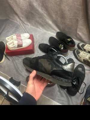 Valentino Rockrunner svarta sneakers - Snygga svarta Valentino Rockrunner sneakers med coolt camouflagemönster och silvriga detaljer vid hälen. Skorna har snörning, platt sula och är tillverkade i en mix av skinn och mocka. Perfekta för dig som vill sticka ut med en exklusiv streetstyle.