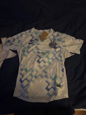 Inter Milan Thuram matchtröja - Säljer en Inter Milan matchtröja från Nike med Thuram och nummer 9 på ryggen. Tröjan är vit med blått geometriskt mönster och har klubbmärket och Nike-loggan på bröstet. Tillverkad i lätt och ventilerande polyester, perfekt för fotboll. Helt ny aldrig använd!