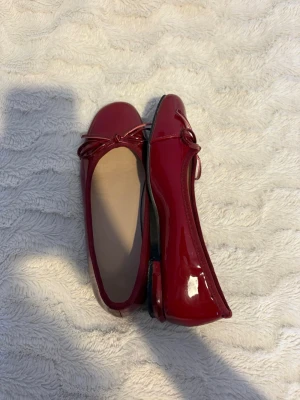Röda ballerinaskor med rosett - Säljer ett par glansiga röda ballerinaskor i storlek 36. Skorna har en söt rosettdetalj framtill och rund tå. Säljer dom för att dom är för stora för mig, använda ute en kväll. 