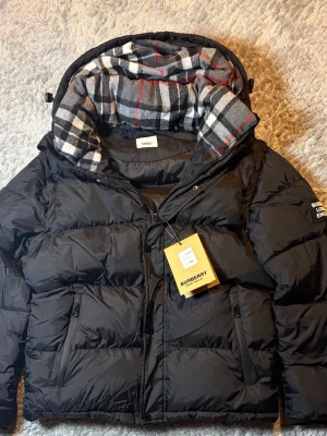 Svart dunjacka från Burberry - Snygg svart dunjacka från Burberry med avtagbara ärmar så den kan användas som väst. Storlek Xl sitter mer som m passar om du är 175-180. Helt ny oanvänd 