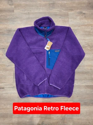 Patagonia Retro Pile Fleece Jacket Purple Boxy Fit Outdoor Vintage - Iconic Patagonia fleece with that unmistakable retro outdoor vibe – bold color, boxy cut, and cozy pile texture that never goes out of style. Patagonia Retro Pile full-zip fleece jacket in deep purple with contrasting blue chest pocket and zips. Perfect for layering, streetwear fits, or everyday outdoor use. ⭐️ ORIGINAL ⭐️  📏 Measurements: Length (A): 72 cm Width / Chest (D): 63 cm Shoulder to cuff (B): 61 cm Pit to cuff (C): 56 cm  ✅ Condition: New with tags ✅ 📐 Size: L