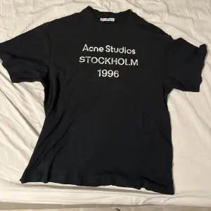 Svart t-shirt från Acne Studios med tryck 'Acne Studios Stockholm 1996' på bröstet. Klassisk rund hals och korta ärmar. Materialet är mjuk bomull och passformen är normal. Perfekt för dig som gillar stilrena och ikoniska plagg. Är använd och köptes på Plick, kvitto finns